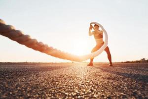 mujer en ropa deportiva entrenando con nudos en la carretera al atardecer foto