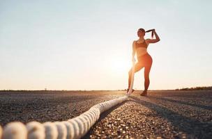 mujer en ropa deportiva entrenando con nudos en la carretera al atardecer foto