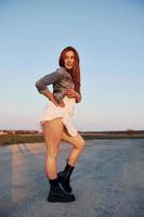 Redhead woman in skirt standing and posing for a camera on the road at evening time photo