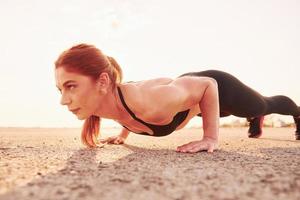 mujer en ropa deportiva haciendo flexiones en la carretera al atardecer foto