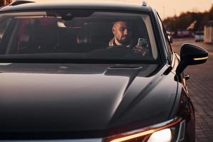 Front view of handsome unshaved man in fashionable clothes that riding his automobile photo