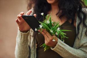 vista de cerca de la mujer que sostiene flores y usa su teléfono inteligente al aire libre foto