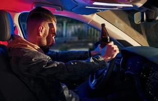 luces de policía negras y rojas. no bebas y manejes. vista lateral de un apuesto hombre sin afeitar con ropa de moda dentro de su automóvil foto