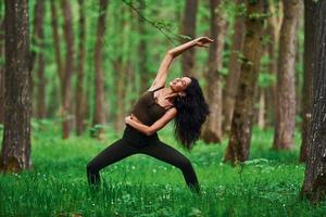 Positive brunette doing fitness outdoors in the forest at daytime photo