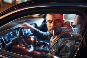 Smoking cigarette. Handsome unshaved man in fashionable clothes riding his automobile photo