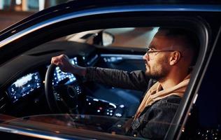 Side view of handsome unshaved man in fashionable clothes that riding his automobile photo