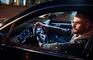 Side view of handsome unshaved man in fashionable clothes that riding his automobile photo
