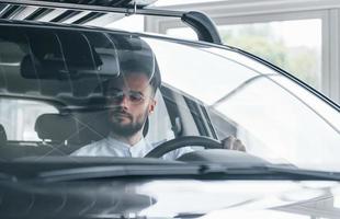 Young handsome man in formal clothes sitting in brand new automobile photo