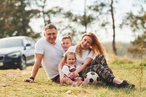 sentado y acostado en el suelo. familia feliz pasando el fin de semana juntos al aire libre cerca del bosque. con hija e hijo foto