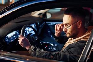 Side view of handsome unshaved man in fashionable clothes that riding his automobile photo