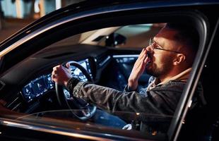 Tired handsome unshaved man in fashionable clothes riding his automobile photo