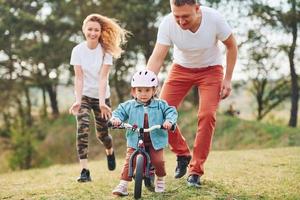 Mother and father teaching daughter how to ride bicycle outdoors photo