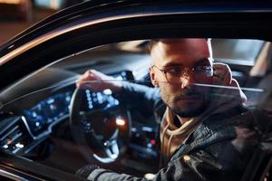 Side view of handsome unshaved man in fashionable clothes that riding his automobile photo