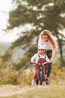 madre con camisa blanca enseñando a su hija a andar en bicicleta al aire libre foto