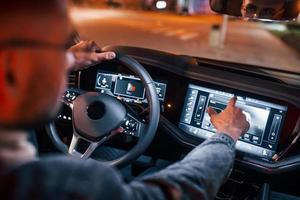 Using navigation display. Handsome unshaved man in fashionable clothes riding his automobile photo