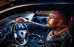 Side view of handsome unshaved man in fashionable clothes that riding his automobile photo