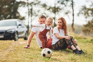 jugando con balón de fútbol. padre y madre pasan el fin de semana al aire libre cerca del bosque con su hija foto