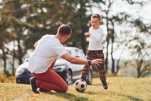 Playing soccer. Father with his son spending weekend together outdoors near forest at daytime photo