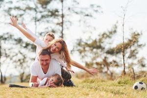 Sitting and lying on the ground. Happy family spending weekend together outdoors near the forest. With daughter and son photo