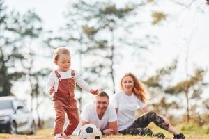 Playing with soccer ball. Father and mother spending weekend outdoors near forest with daughter photo