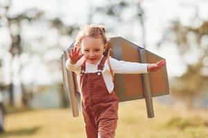 Cute little girl with handmaded wings running outdoors on the field and having fun photo