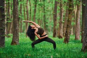 Positive brunette doing fitness outdoors in the forest at daytime photo