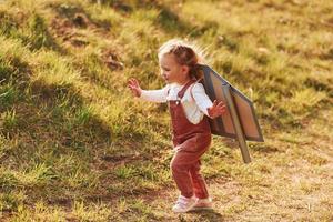 Cute little girl with handmaded wings running outdoors on the field and having fun photo