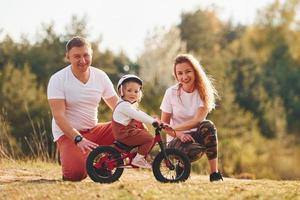 Mother and father teaching daughter how to ride bicycle outdoors photo