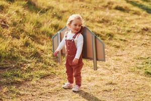 Cute little girl with handmaded wings running outdoors on the field and having fun photo