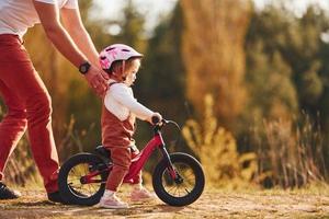 hermosa luz del sol. padre con camisa blanca enseñando a su hija a andar en bicicleta al aire libre foto