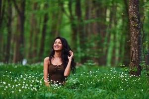 Positive brunette in casual clothes sitting in the forest at daytime photo