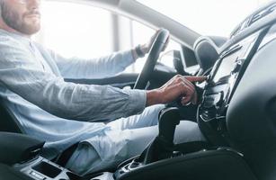 Side view of young handsome man in formal clothes that sitting in brand new automobile photo