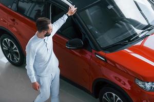 Young elegant man in white formal clothes standing near red automobile photo