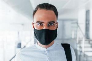In protective mask and gloves. Young handsome man in formal clothes indoors in the office at daytime photo