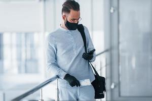 In protective mask and gloves. Young handsome man in formal clothes indoors in the office at daytime photo