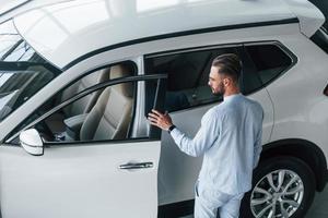 Young elegant man in white formal clothes standing near white automobile photo