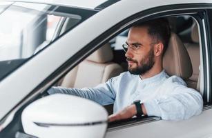 Side view of young handsome man in formal clothes that sitting in brand new automobile photo