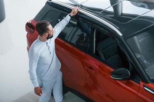 Young elegant man in white formal clothes standing near red automobile photo