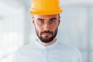 Portrait of engineer in orange protective hard hat and glasses that standing and working indoors