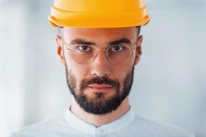 Portrait of engineer in orange protective hard hat and glasses that standing and working indoors photo