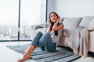 joven mujer hermosa con ropa informal sentada sola en casa y escuchando música con auriculares foto