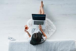 Top view of young woman in casual clothes that sitting at home alone with laptop and tea photo