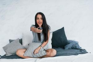 sosteniendo el control remoto de la televisión y viendo películas. mujer hermosa joven en ropa casual sentada en casa sola foto