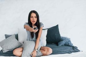 sosteniendo el control remoto de la televisión y viendo películas. mujer hermosa joven en ropa casual sentada en casa sola foto