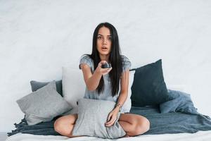 sosteniendo el control remoto de la televisión y viendo películas. mujer hermosa joven en ropa casual sentada en casa sola foto