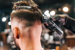 Close up view of young bearded man that sitting and getting haircut in barber shop photo