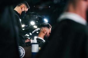 Young bearded man sitting and getting haircut in barber shop photo