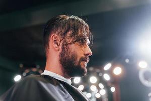 Young bearded man sitting in barber shop and waiting for stylist photo