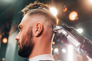 Close up view of young bearded man that sitting and getting haircut in barber shop photo