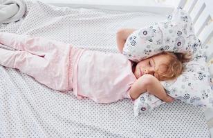 Lying down on the bed. Cute little girl in casual clothes is indoors at home at daytime photo